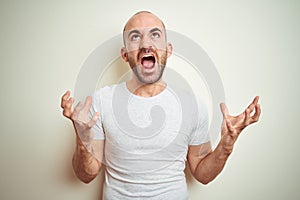 Young bald man with beard wearing casual white t-shirt over isolated background crazy and mad shouting and yelling with aggressive