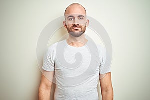 Young bald man with beard wearing casual white t-shirt over isolated background with serious expression on face