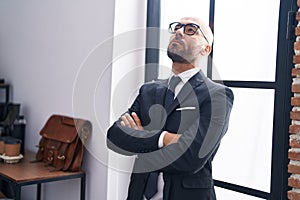 Young bald man business worker standing with arms crossed gesture and serious expression at office