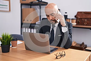 Young bald man business worker using laptop talking on smartphone at office