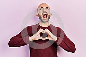 Young bald man doing heart symbol with hands angry and mad screaming frustrated and furious, shouting with anger looking up