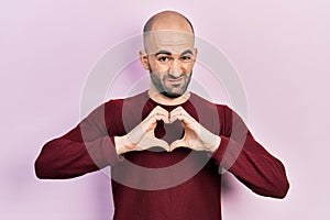 Young bald man doing heart symbol with hands clueless and confused expression