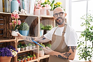 Young bald man florist using touchpad holding plant at florist