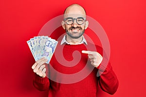 Young bald man holding 100 romanian leu banknotes smiling happy pointing with hand and finger