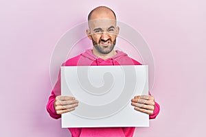 Young bald man holding blank empty banner clueless and confused expression