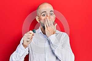 Young bald man holding sdxc card covering mouth with hand, shocked and afraid for mistake