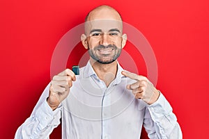 Young bald man holding sdxc card smiling happy pointing with hand and finger