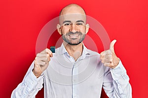 Young bald man holding sdxc card smiling happy and positive, thumb up doing excellent and approval sign