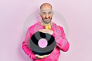 Young bald man holding vinyl disc clueless and confused expression