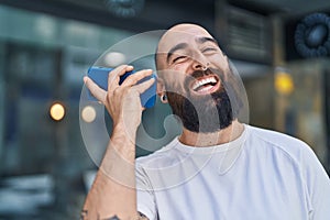 Young bald man miling confident listening audio message by the smartphone at street