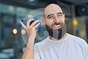 Young bald man miling confident listening audio message by the smartphone at street