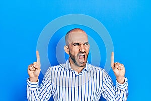 Young bald man pointing up with fingers angry and mad screaming frustrated and furious, shouting with anger