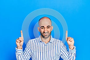 Young bald man pointing up with fingers clueless and confused expression