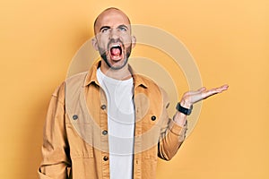 Young bald man presenting with open palms, holding something angry and mad screaming frustrated and furious, shouting with anger