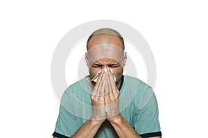 Young bald man sick from common cold flu blowing his nose with paper tissue isolated on white background.