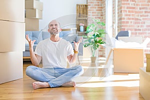 Young bald man sitting on the floor around cardboard boxes moving to a new home crazy and mad shouting and yelling with aggressive