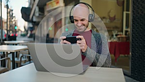 Young bald man smiling confident playing video game at coffee shop terrace