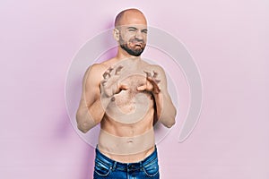 Young bald man standing shirtless disgusted expression, displeased and fearful doing disgust face because aversion reaction