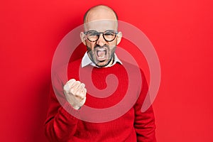 Young bald man wearing casual clothes and glasses angry and mad raising fist frustrated and furious while shouting with anger