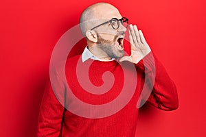 Young bald man wearing casual clothes and glasses shouting and screaming loud to side with hand on mouth