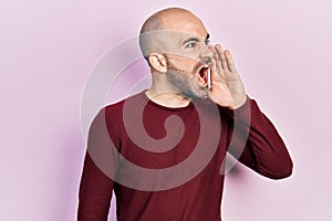 Young bald man wearing casual clothes shouting and screaming loud to side with hand on mouth