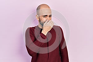 Young bald man wearing casual clothes smelling something stinky and disgusting, intolerable smell, holding breath with fingers on