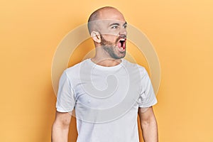 Young bald man wearing casual white t shirt angry and mad screaming frustrated and furious, shouting with anger