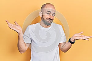 Young bald man wearing casual white t shirt clueless and confused expression with arms and hands raised