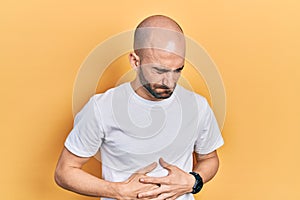 Young bald man wearing casual white t shirt with hand on stomach because indigestion, painful illness feeling unwell