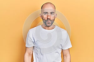 Young bald man wearing casual white t shirt making fish face with lips, crazy and comical gesture