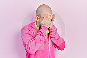 Young bald man wearing gym clothes and using headphones with sad expression covering face with hands while crying