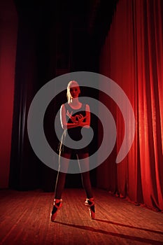 Young ballerina in black clothe on stage with red curtains