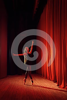 Young ballerina in black clothe on stage with red curtains