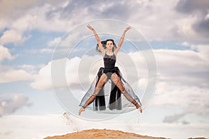 young ballerina in a black long dress soars in a jump above the ground