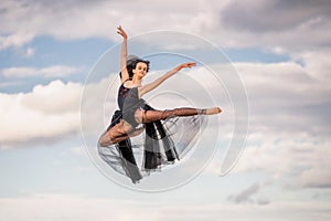 Young ballerina in a black long dress soars in a jump above the ground
