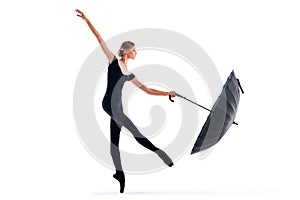 A young ballerina in black pointe shoes and leotard posing with umbrella in graceful pose isolated on white background