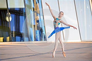 Young ballerina in a bright blue tutu is dancing against backdrop of cityscape