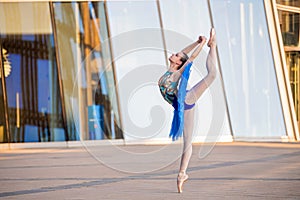 Young ballerina in a bright blue tutu is dancing against backdrop of cityscape