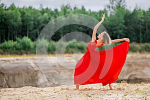 Young ballerina in a bright red long dress soars in a jump above the ground