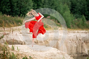 Young ballerina in a bright red long dress soars in a jump above the ground