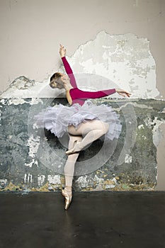 Young ballerina dancer dancing classical ballet against rustic wall