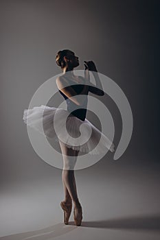 Young ballerina in elegance white tutu and pointe shoes dancing against dark background