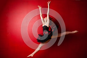 Young ballerina executing a jump against bright red wall