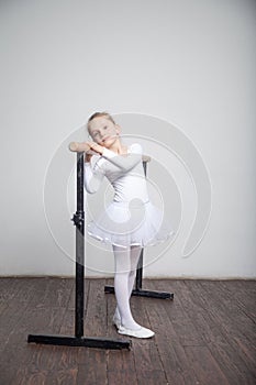 Young ballerina girl in a white tutu. Adorable child dancing classical ballet in a white studio with wooden floor. Children dance.