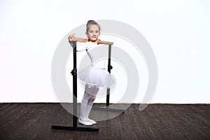 Young ballerina girl in a white tutu. Adorable child dancing classical ballet in a white studio with wooden floor. Children dance.