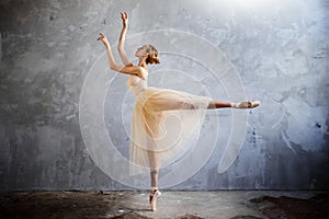 Young ballerina in a golden colored dancing costume is posing in a loft studio