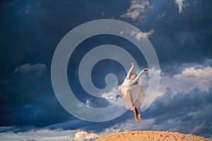 Young ballerina in a light long white dress flies in a jump