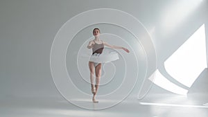 Young ballerina in pointe shoes and white ballet tutu makes pirouette. Shot on a white background in the spacious and