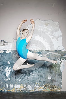 Young ballerina is posing and dancing classical ballet against rustic wall