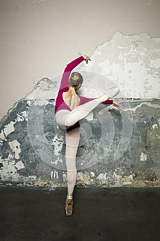 Young ballerina is posing and dancing classical ballet against rustic wall